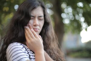 Woman holding cheek due to tooth sensitivity and dental pain