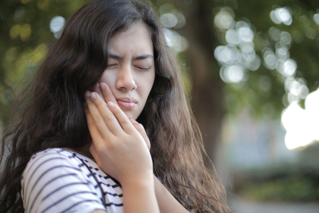 Woman holding cheek due to tooth sensitivity and dental pain